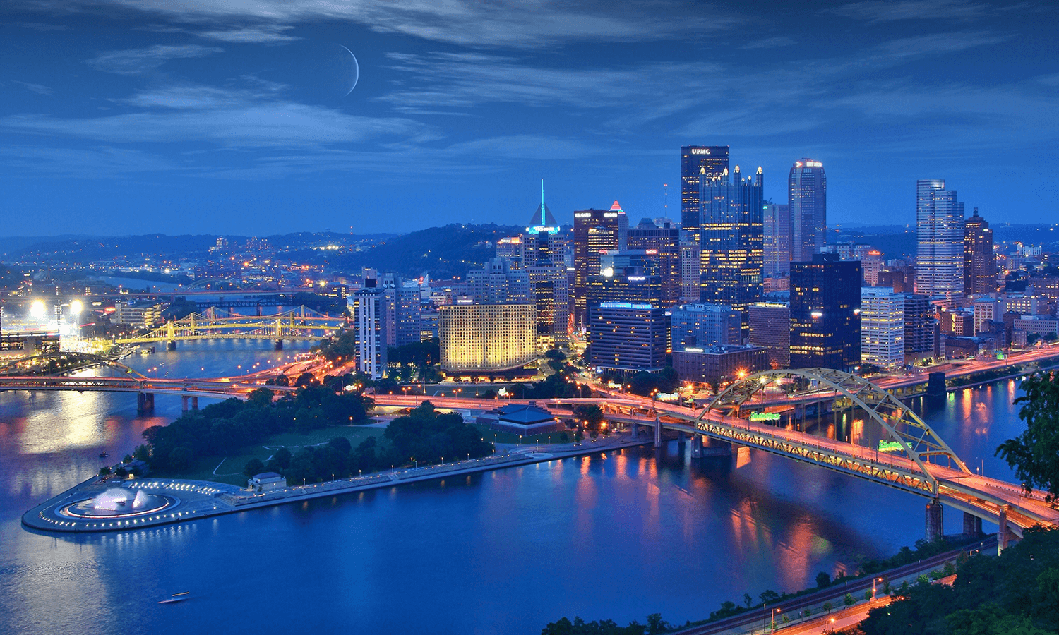 Downtown Pittsburgh skyline and bridges illuminated at dusk along the rivers