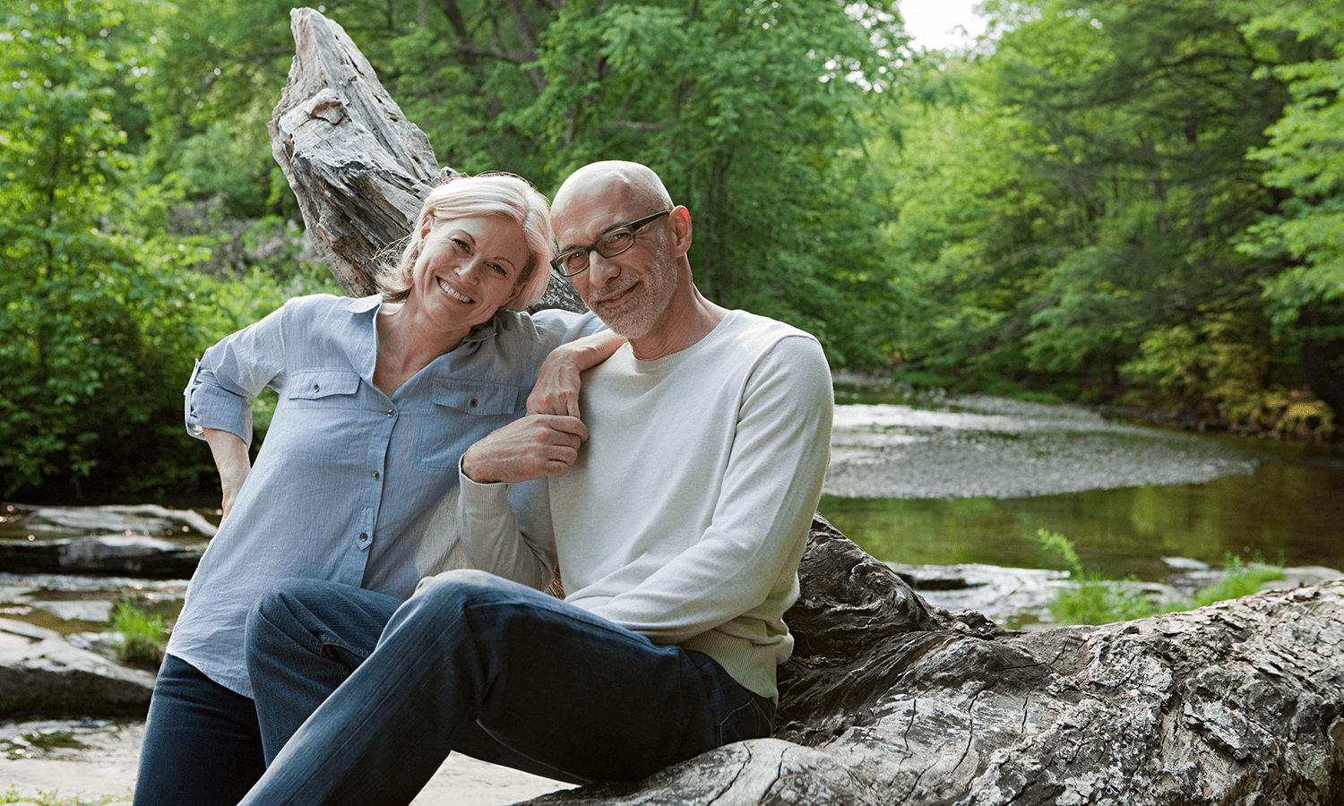 Smiling retired couple relaxing together by a peaceful wooded river