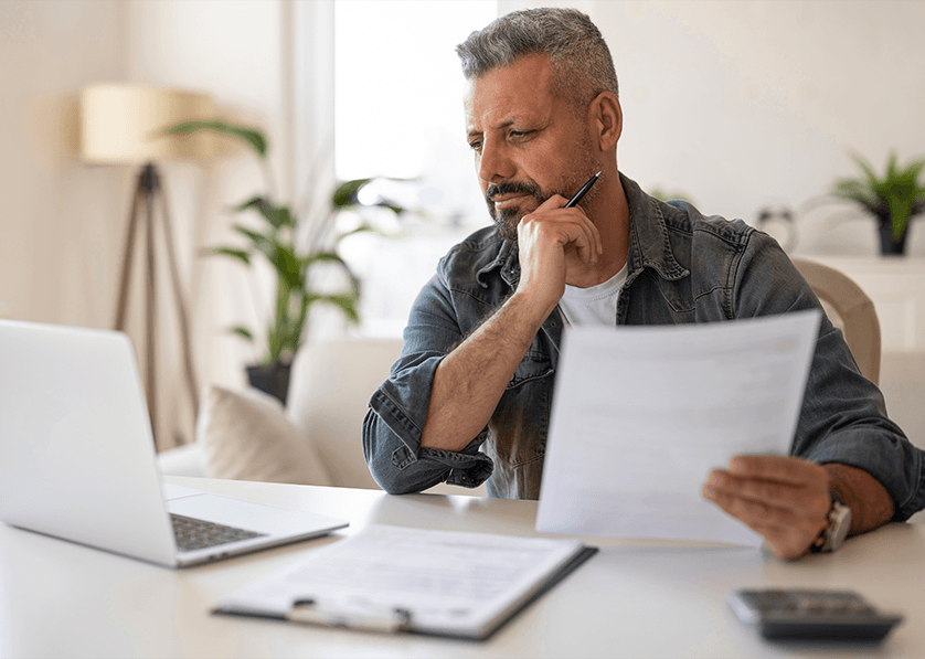 Man reviewing financial documents and expenses on a laptop at home