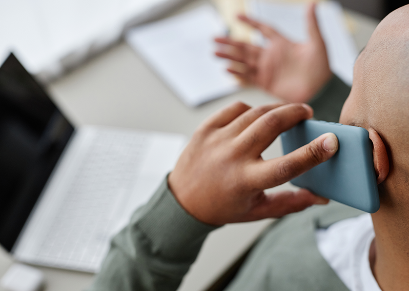 Person using a smartphone while working on a laptop at home